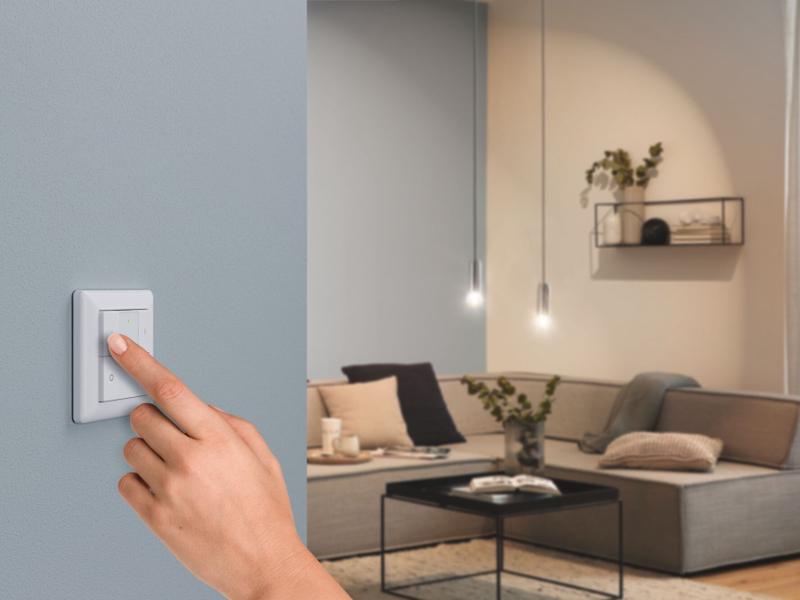 Hand bedient weißen Wand-Dimmer-Schalter in modernem Wohnzimmer mit grauer Couch und Pendelleuchten.