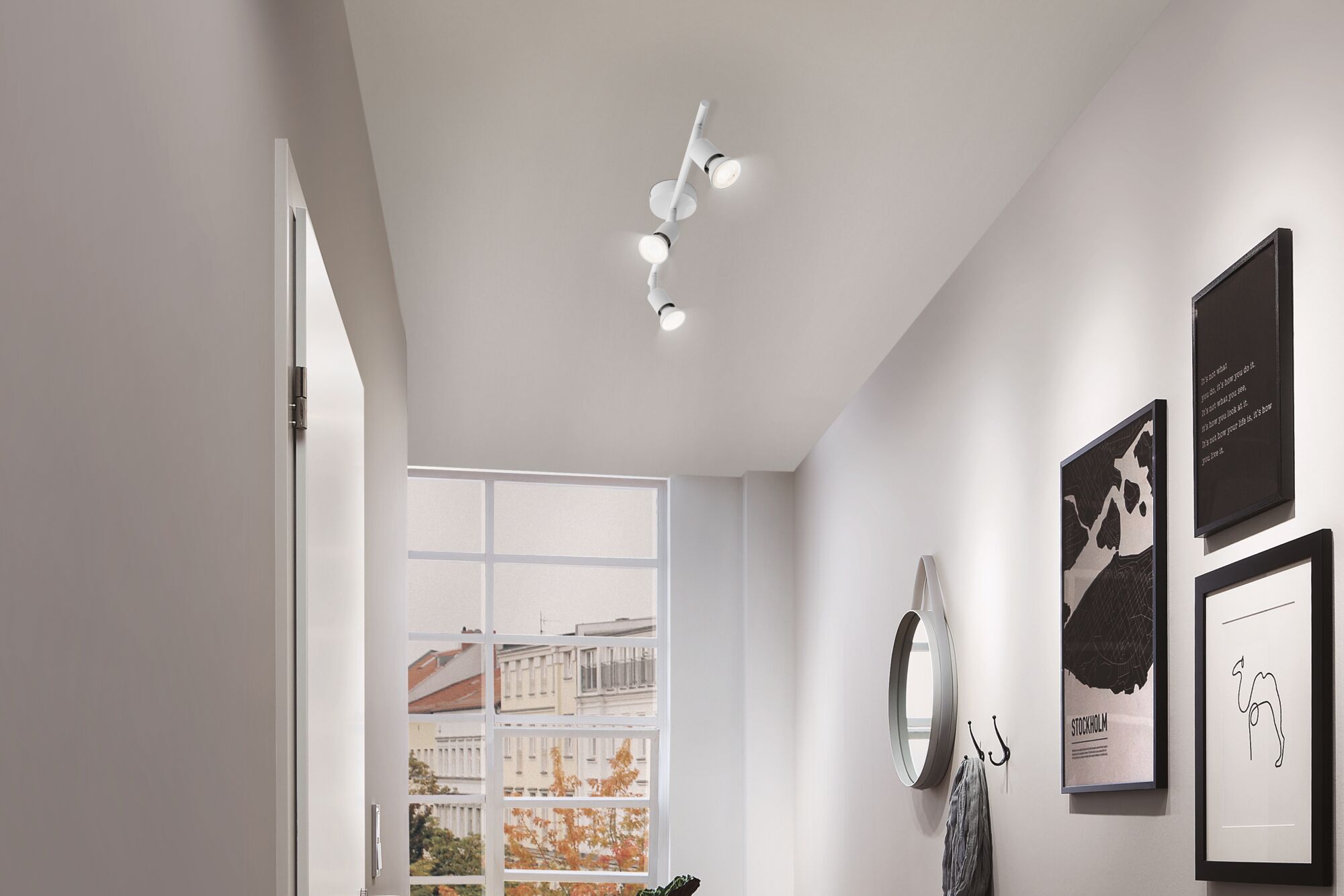 Moderne witte plafondspot met drie LED-lampen in hal met spiegel en wanddecoratie.