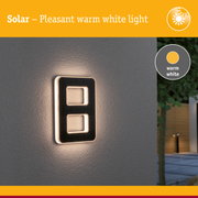 Solar outdoor wall light with warm white illumination and sleek black design mounted on grey wall