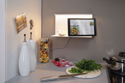 Weiße Wandlampe mit Ablage und Tablet-Halterung in moderner Küche mit Kräutern und Pasta.