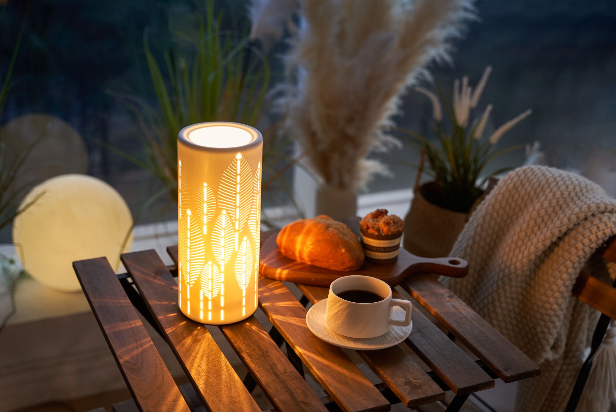 Lampe de table en céramique avec lumière chaude et motif feuilles sur table en bois avec café et pâtisseries