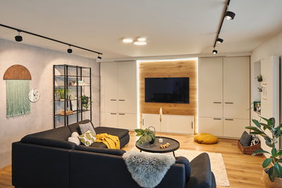 Moderne woonkamer met zwarte bank, houten tv-wand en LED-plafondspots voor sfeerverlichting