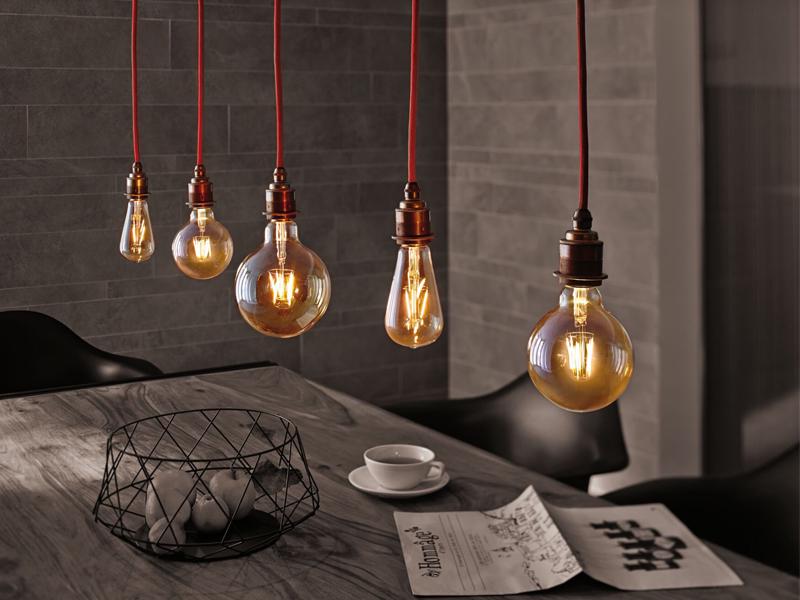 Cinq ampoules à filament suspendues avec lumière chaude au-dessus d'une table en bois avec journal et tasse dans une pièce moderne.