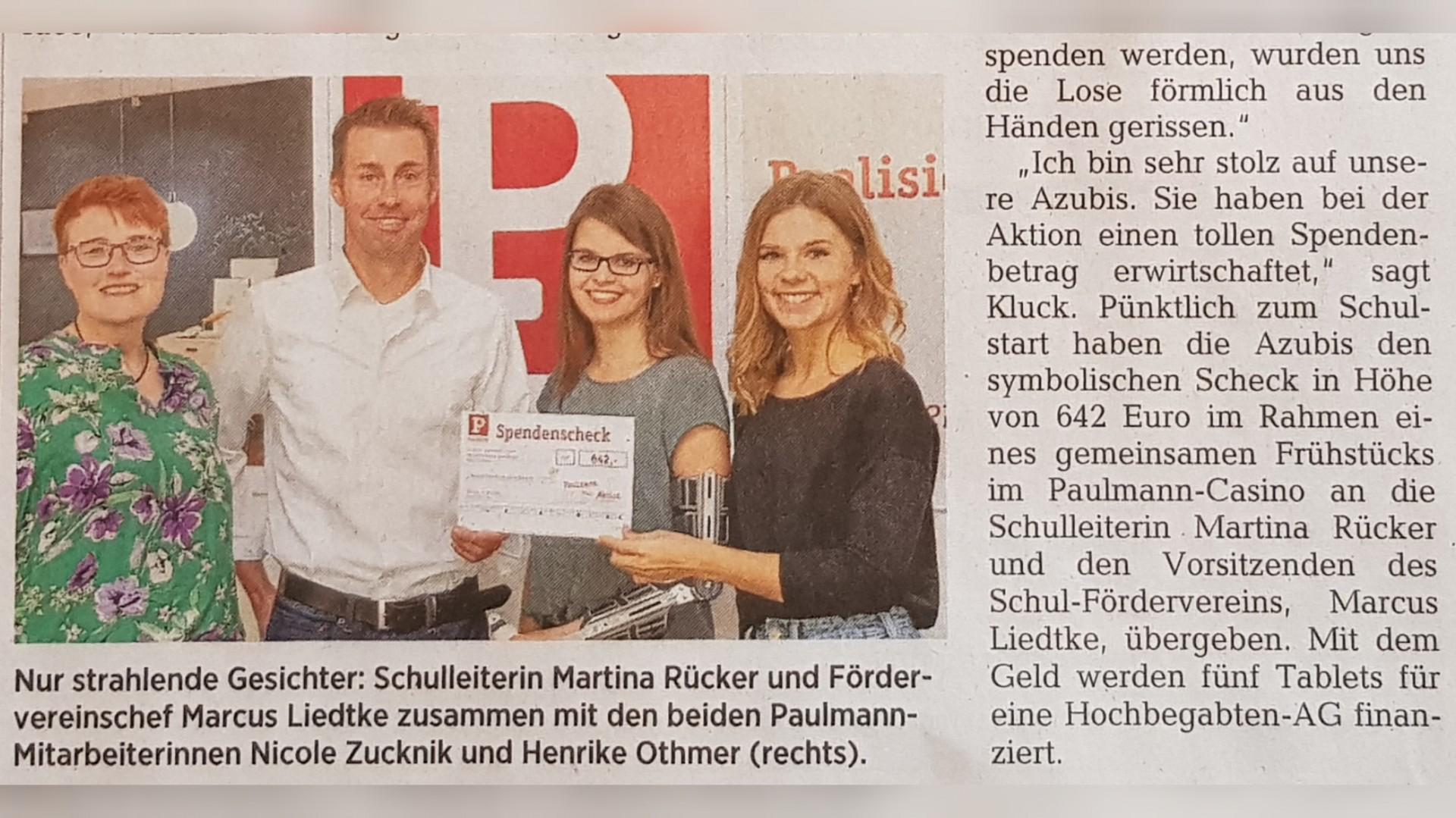 Vier Personen übergeben symbolischen Spendenscheck bei Paulmann, Aktion für Tablets an Schule.