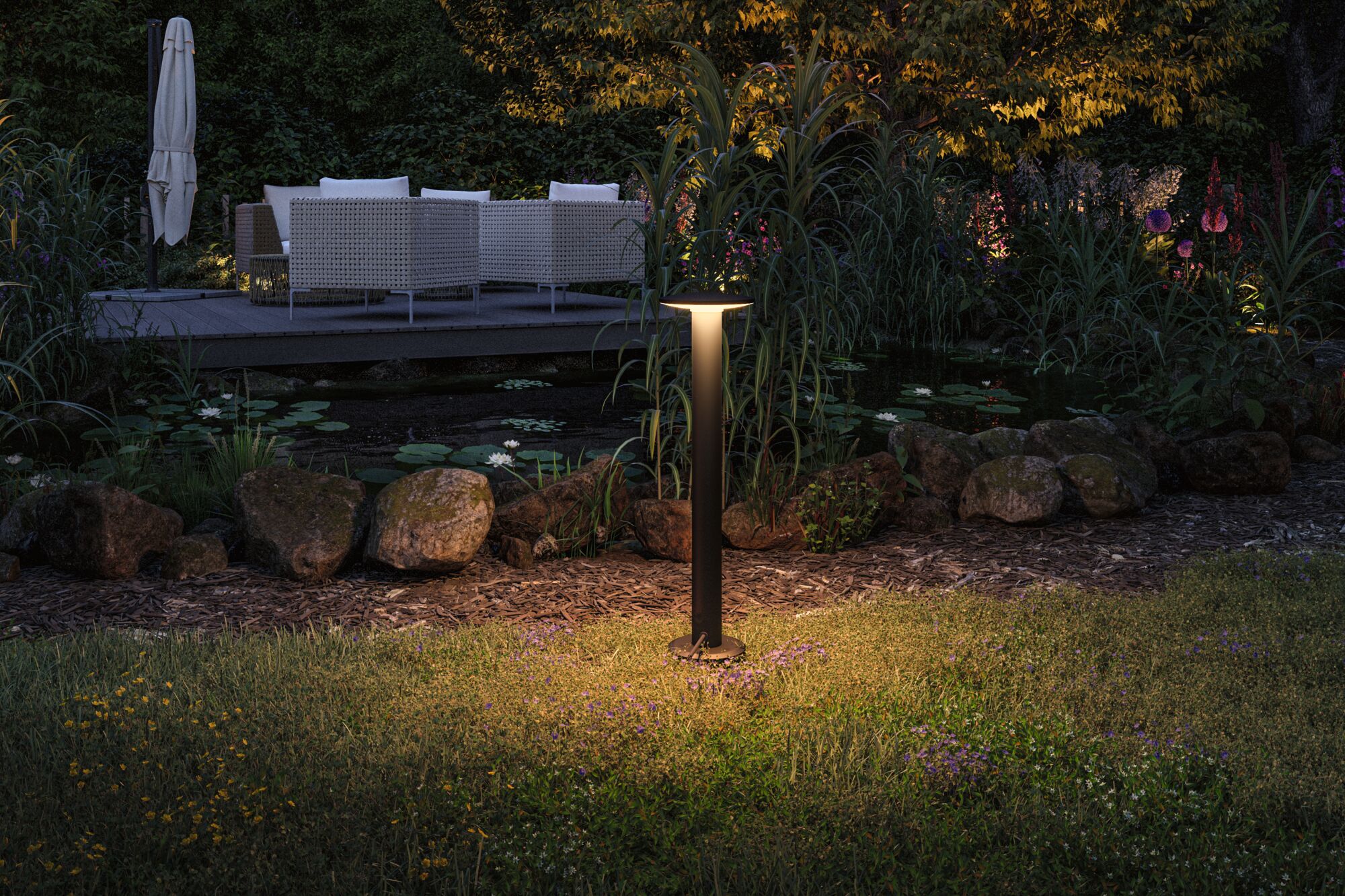 Black metal LED garden light illuminating grass and plants near pond and patio in nighttime outdoor setting