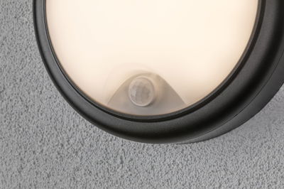 Nahaufnahme einer runden Außenwandleuchte mit schwarzem Rahmen und warmweißem Licht an grauer Wand