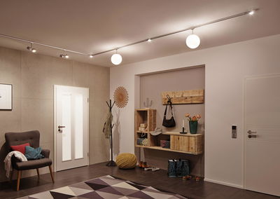 Moderne hal met houten plank, fauteuil, vloerkleed en plafondlamp met witte bollen en spots