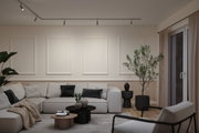 Modern living room with beige sectional sofa, black and grey cushions, wooden and black coffee tables, plants, and ceiling spotlights