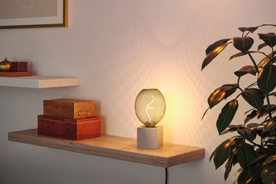 Modern table lamp with white base and green mesh glass casting warm light and decorative shadows.