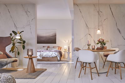 Modern living room with white wooden floor, round dining table, white chairs, and marble wall decor.