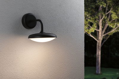 Schwarze Außenwandleuchte aus Metall mit warmweißem Licht an grauer Wand im Garten