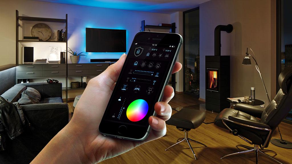Smartphone steuert farbige LED-Beleuchtung in modernem Wohnzimmer mit Kamin und Ledersessel.