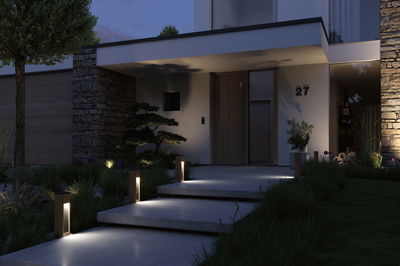 Moderne Außenbeleuchtung mit warmweißen LED-Pfostenleuchten aus Holz an Hauseingang mit Treppe.