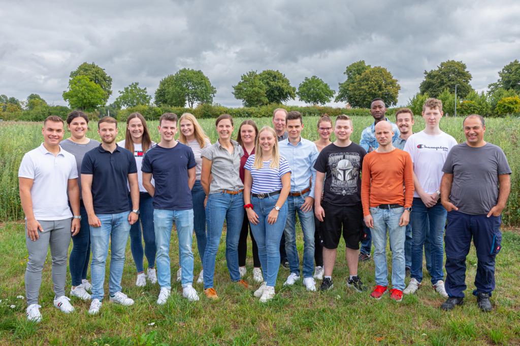 Gruppe junger Auszubildender und Mitarbeiter im Freien vor grüner Landschaft, Teamfoto für Karriere und Ausbildung.