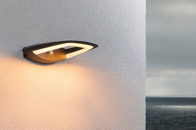 Moderne schwarze Außenwandleuchte aus Metall mit warmweißem LED-Licht an weißer Wand und Meerblick