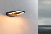 Moderne schwarze LED-Wandleuchte mit warmweißem Licht an weißer Außenwand mit Meerblick