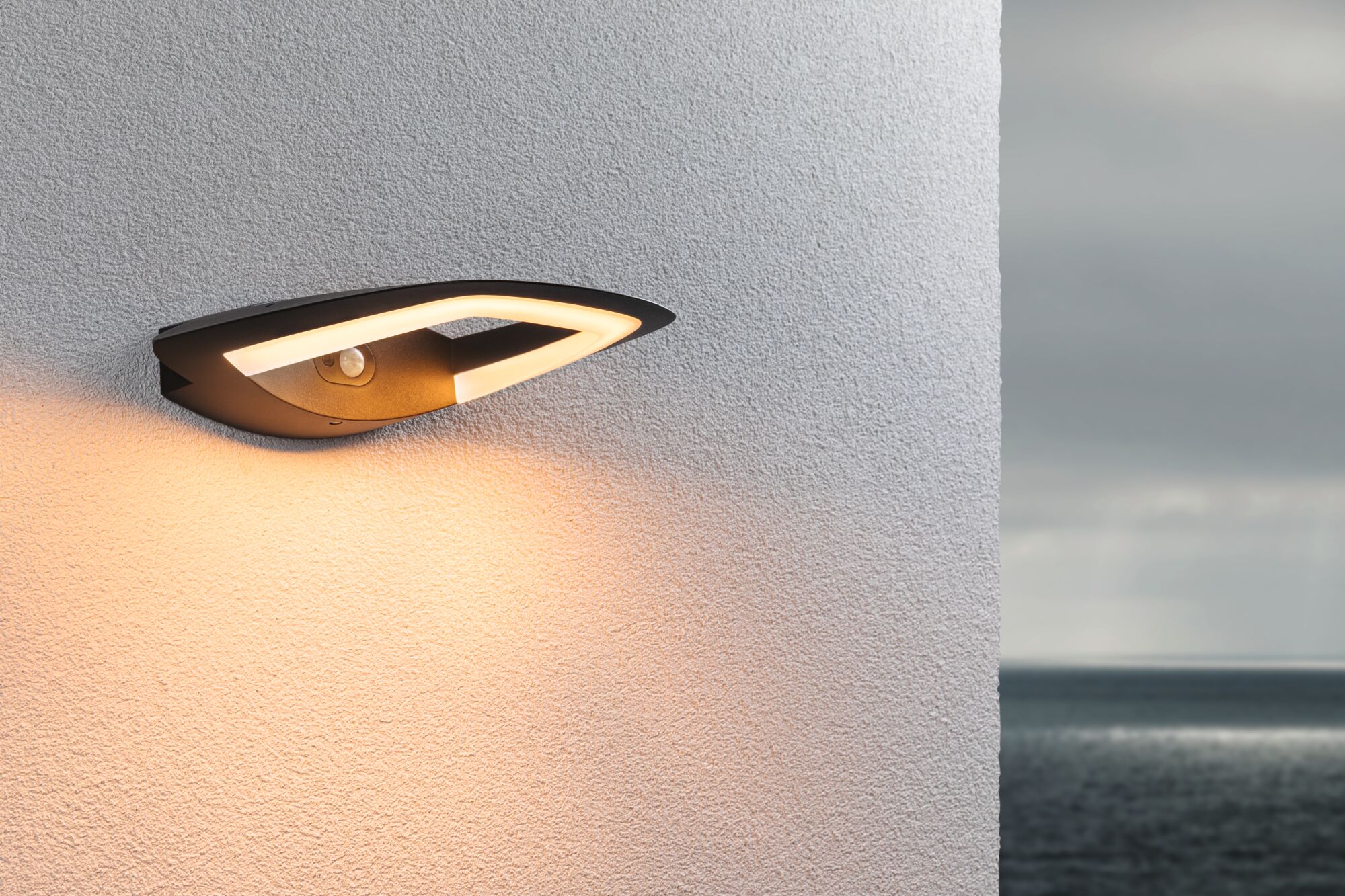 Moderne schwarze LED-Wandleuchte mit warmweißem Licht an weißer Außenwand mit Meerblick
