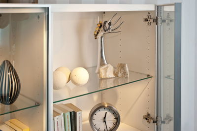 White decorative balls and silver jewelry holder in illuminated glass cabinet with clock and books