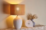 Lampe de table en céramique blanche à design côtelé avec abat-jour marron à côté d'une horloge en marbre blanc et vase gris