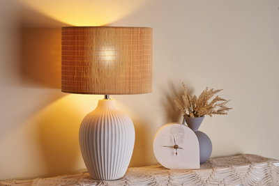 Weiße Keramik-Tischlampe mit geripptem Design und braunem Lampenschirm neben weißer Marmor-Uhr und grauer Vase