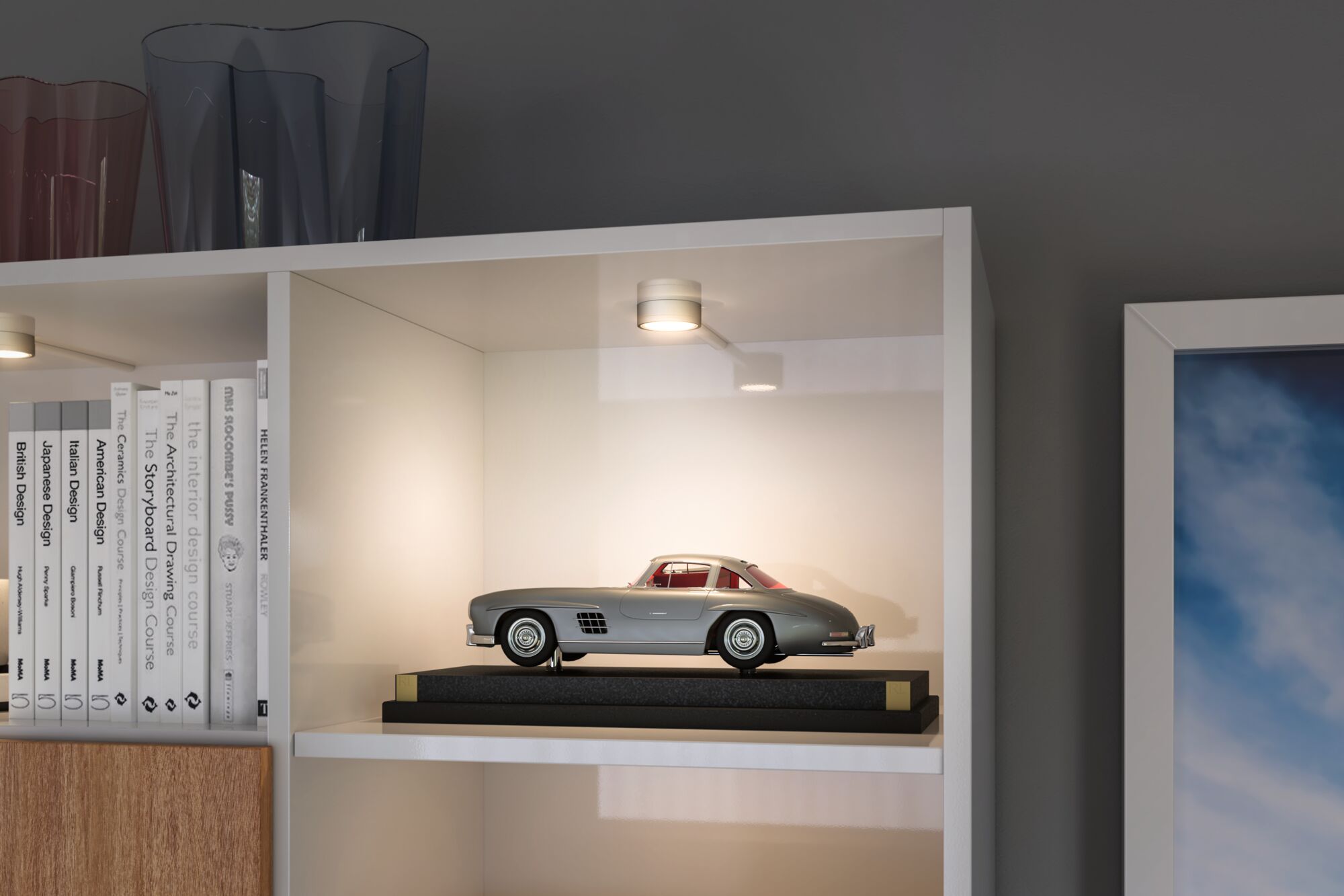 Kleine grijze modelauto op zwarte standaard verlicht door witte LED-plafondspot in kast.