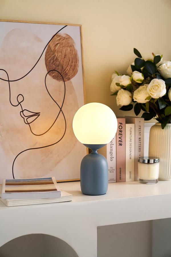 Modern table lamp with round frosted glass and matte grey metal base on white sideboard with decor.