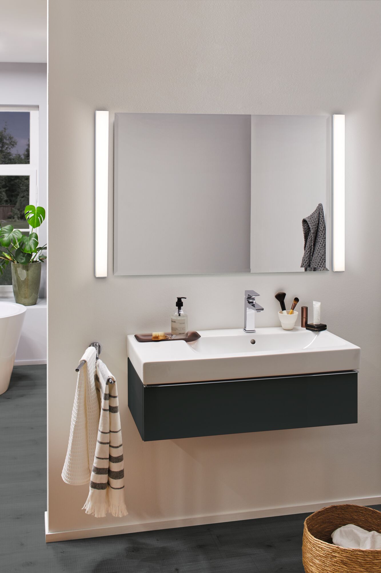 Salle de bain moderne avec lavabo en céramique blanc et meuble noir, éclairée par deux appliques LED murales.