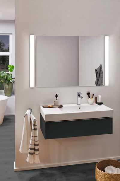 Salle de bain moderne avec lavabo en céramique blanc et meuble noir, éclairée par deux appliques LED murales.