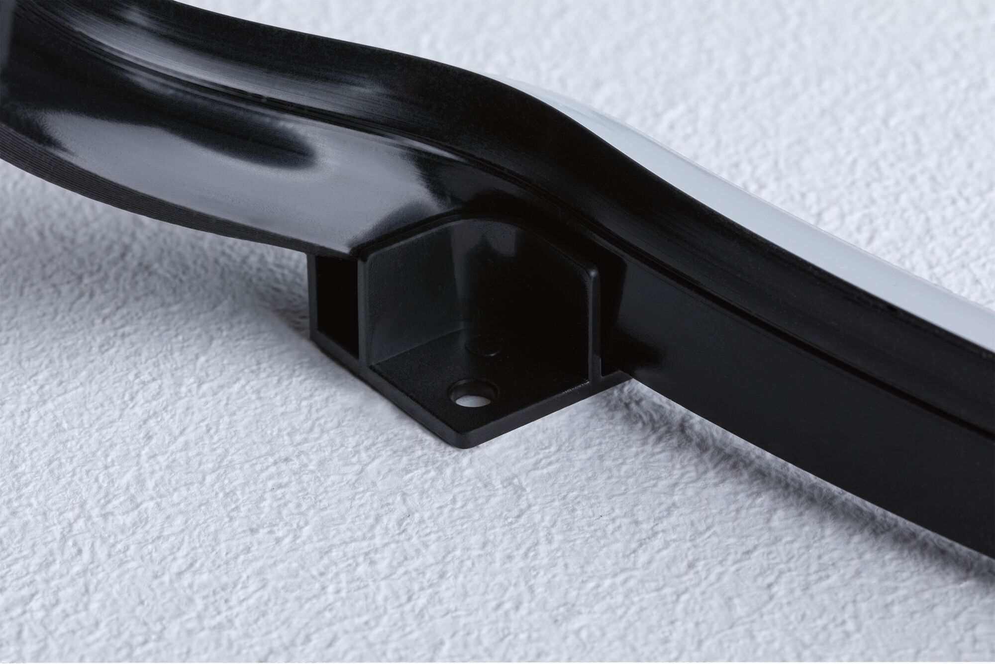 Black plastic mounting bracket with screw hole on white surface for LED lighting fixture.