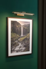 Applique LED moderne en métal brossé sur mur vert au-dessus d'une photo de paysage avec cascade.