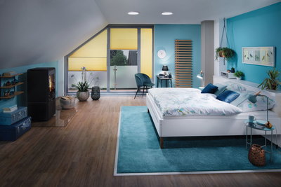 Modernes Schlafzimmer mit weißem Bett, blauem Teppich und gelben Plissees, Holzfußboden und Kaminofen.