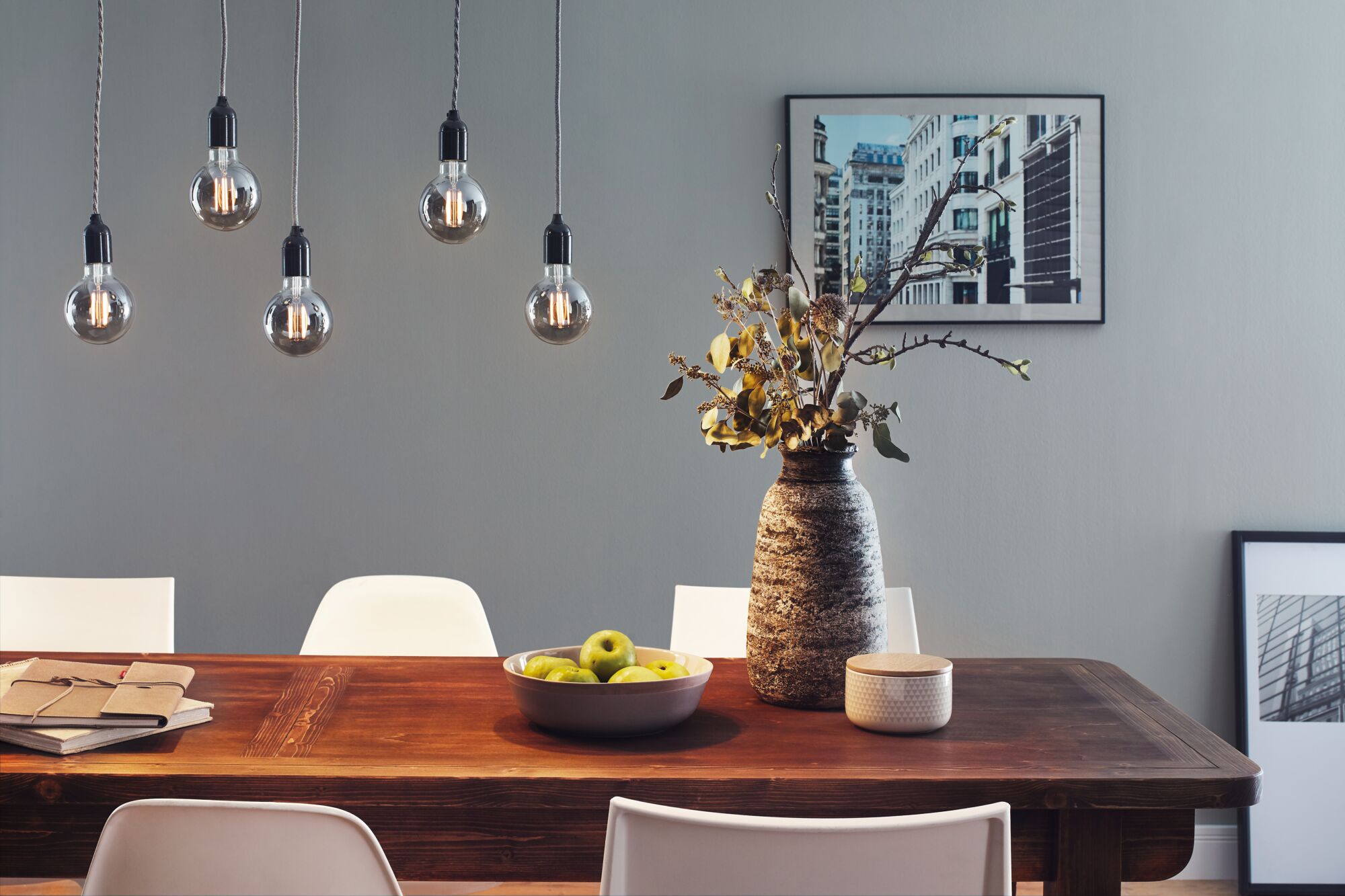 Five LED filament bulbs with smoked glass hanging over wooden dining table with vase and green fruit