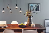 Vijf LED-gloeilampen met rookglas hangend boven houten eettafel met vaas en groen fruit