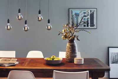 Vijf LED-gloeilampen met rookglas hangend boven houten eettafel met vaas en groen fruit