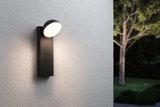 Modern black metal LED wall light with round diffuser mounted on white exterior wall