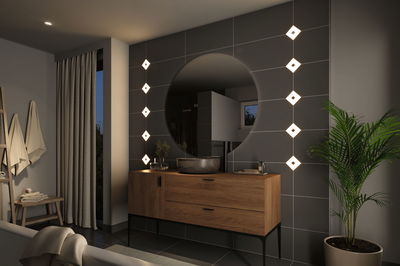 Moderne badkamer met houten wastafelmeubel, ronde spiegel en warmwitte LED-wandlampen.