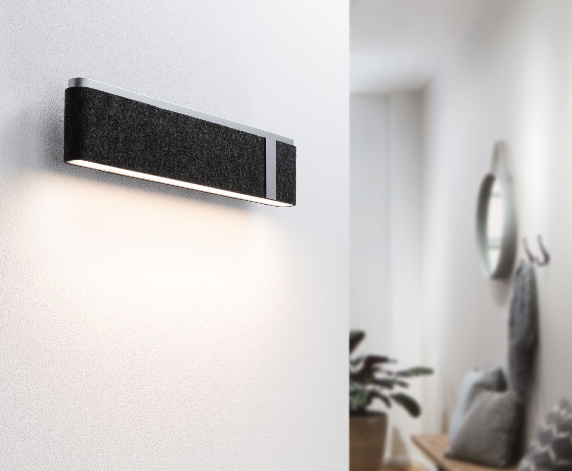 Moderne wandlamp met zwarte vilten bekleding en aluminium frame verlicht stijlvolle witte gang.