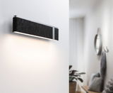 Moderne wandlamp met zwarte vilten bekleding en aluminium frame verlicht stijlvolle witte gang.