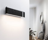 Modern wall light with black felt cover and aluminum frame illuminating white hallway stylishly.