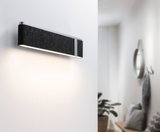 Modern wall light with black felt cover and aluminum frame illuminating white hallway stylishly.