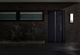 Modernes Haus mit dunkler Tür und beleuchtetem rechteckigem LED-Hausnummernschild an Backsteinwand