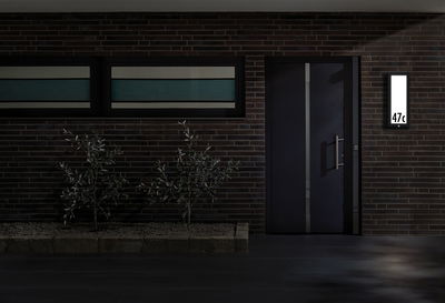Modernes Haus mit dunkler Tür und beleuchtetem rechteckigem LED-Hausnummernschild an Backsteinwand