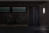Modern house entrance with dark door and illuminated rectangular LED house number sign on brick wall