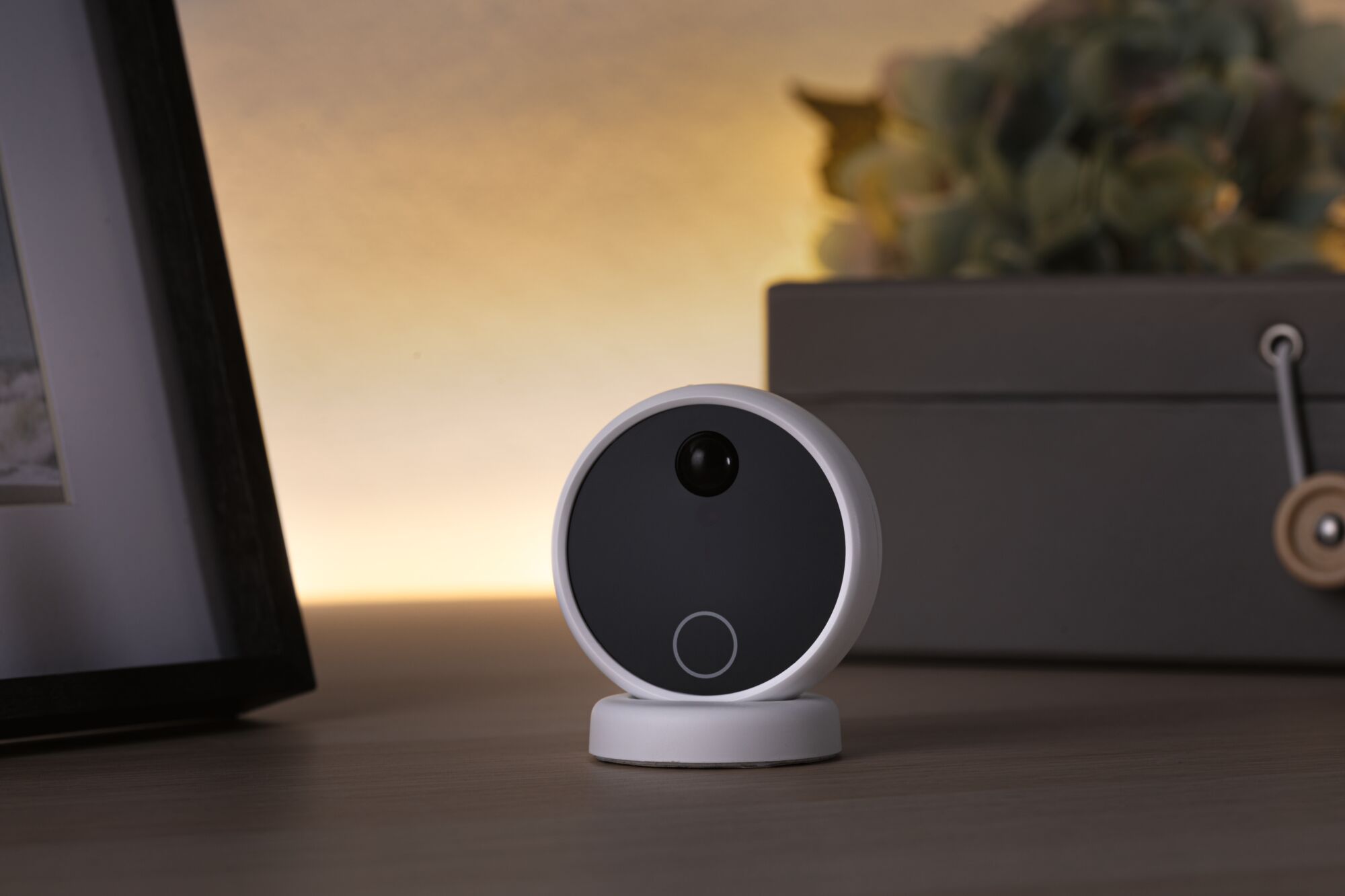 Round white security camera with black front on wooden table, modern home surveillance device.
