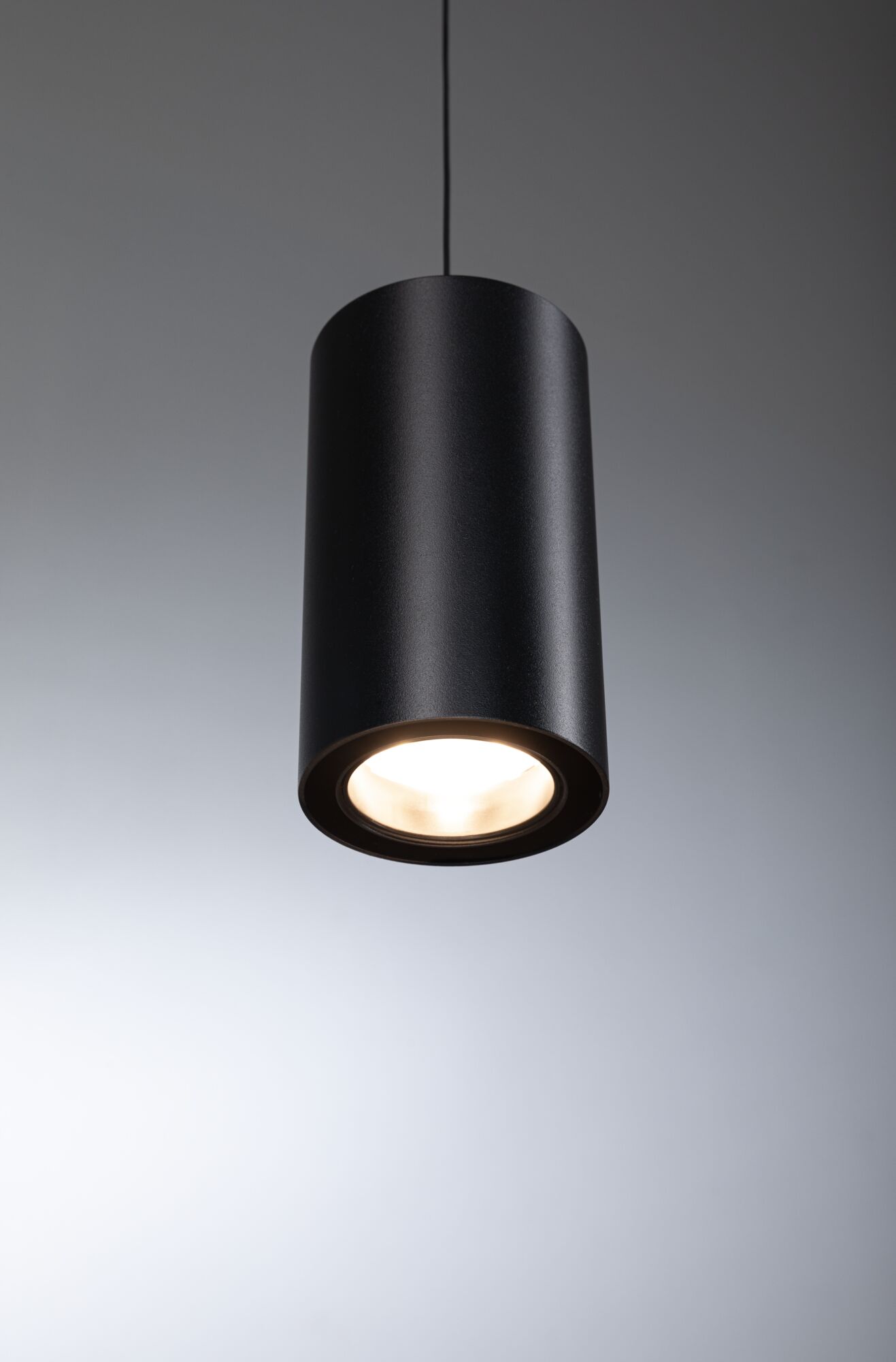 Black cylindrical metal LED pendant light with warm white illumination for modern interiors