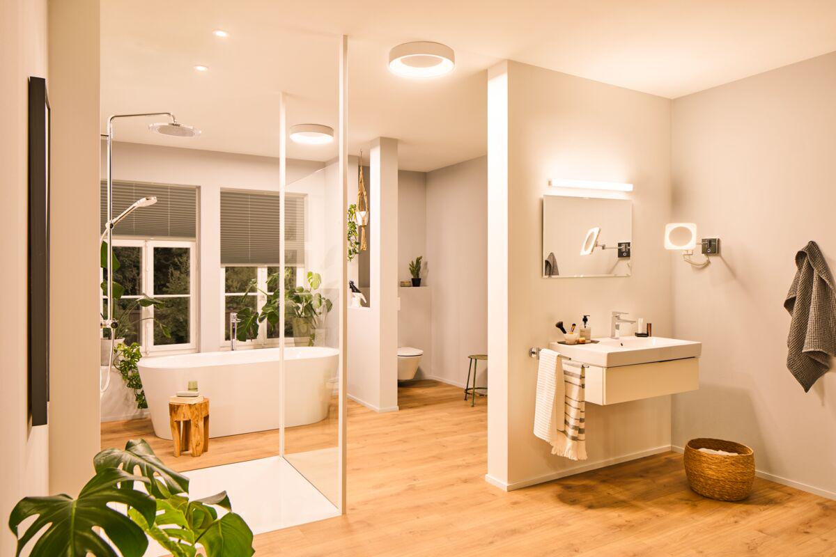 Modern bathroom with warm white ceiling light and mirror lighting, wooden floor and green plants