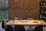 Salle à manger moderne avec table en bois, chaises noires et trois suspensions LED noires sur mur en briques.