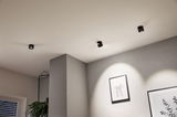 Three black metal LED ceiling spotlights illuminate modern wall with plant pictures in living room.