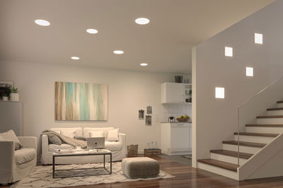 Modern living room with white recessed ceiling lights and square wall lamps on staircase