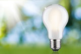 Glowing white light bulb with metal base against blurred green-blue background, energy-saving lamp